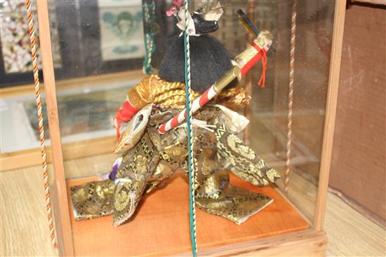 A Japanese wooden cased model of a Samurai warrior holding aloft a fan, with ornate silkwork robes, overall height 35cm, width 33cm